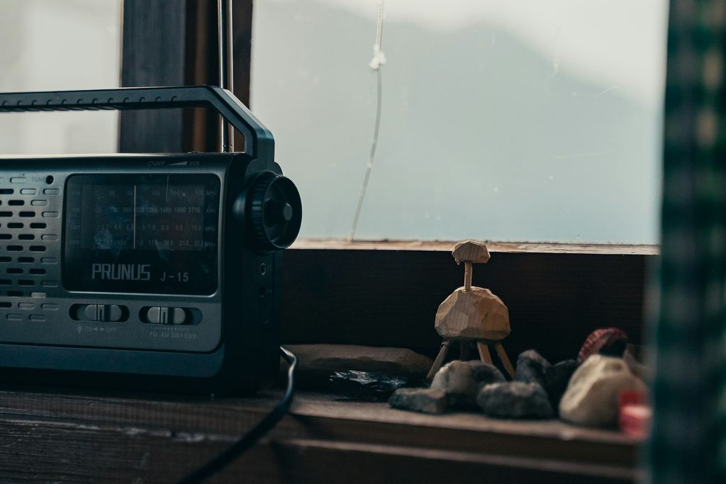 Bärbar radio med antenn på en träfönsterbräda i en stuga, med dimmiga berg utanför fönstret