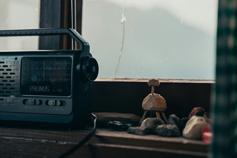 Bärbar radio med antenn på en träfönsterbräda i en stuga, med dimmiga berg utanför fönstret